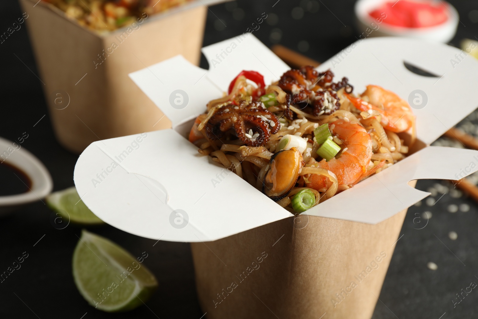 Photo of Box of wok noodles with seafood on black table, closeup