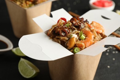 Photo of Box of wok noodles with seafood on black table, closeup