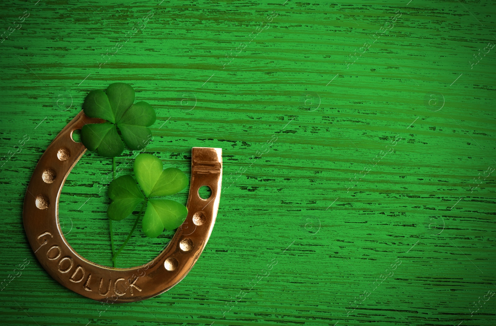 Image of Clover leaves and horseshoe on green wooden table, flat lay with space for text. St. Patrick's Day celebration