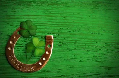 Clover leaves and horseshoe on green wooden table, flat lay with space for text. St. Patrick's Day celebration