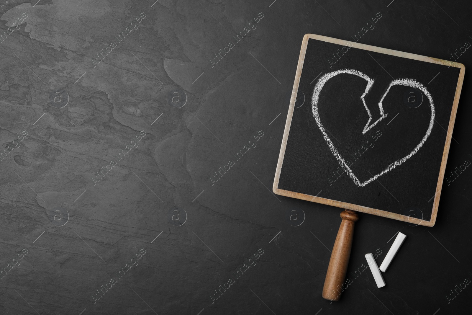 Photo of Blackboard with drawn broken heart and pieces of chalk on dark background, flat lay. Relationship problems concept