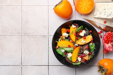 Photo of Delicious persimmon salad with pomegranate and spinach on tiled surface, flat lay. Space for text