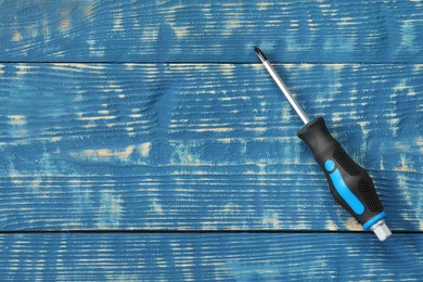 Photo of Screwdriver with black handle on blue wooden table, top view. Space for text