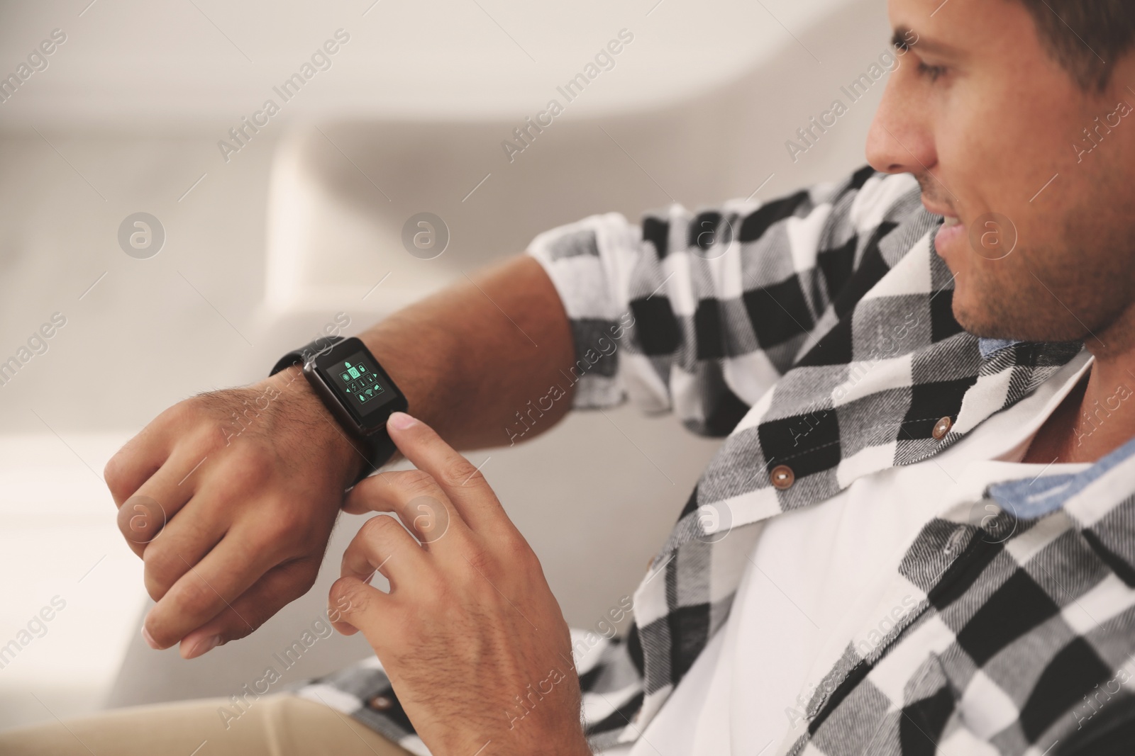 Image of Man setting smart home control system via smartwatch indoors. App interface with icons on display