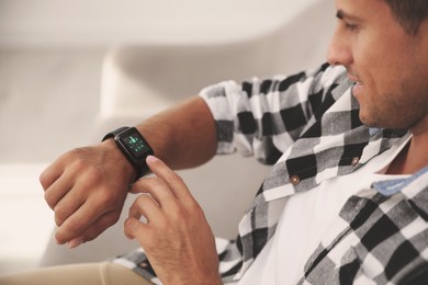 Man setting smart home control system via smartwatch indoors. App interface with icons on display