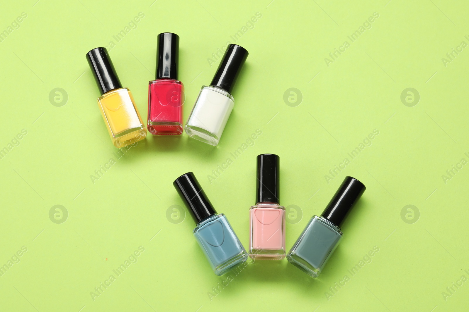 Photo of Colorful nail polishes in bottles on green background, flat lay