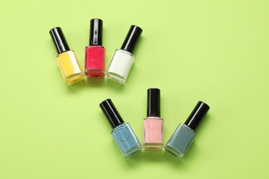 Colorful nail polishes in bottles on green background, flat lay