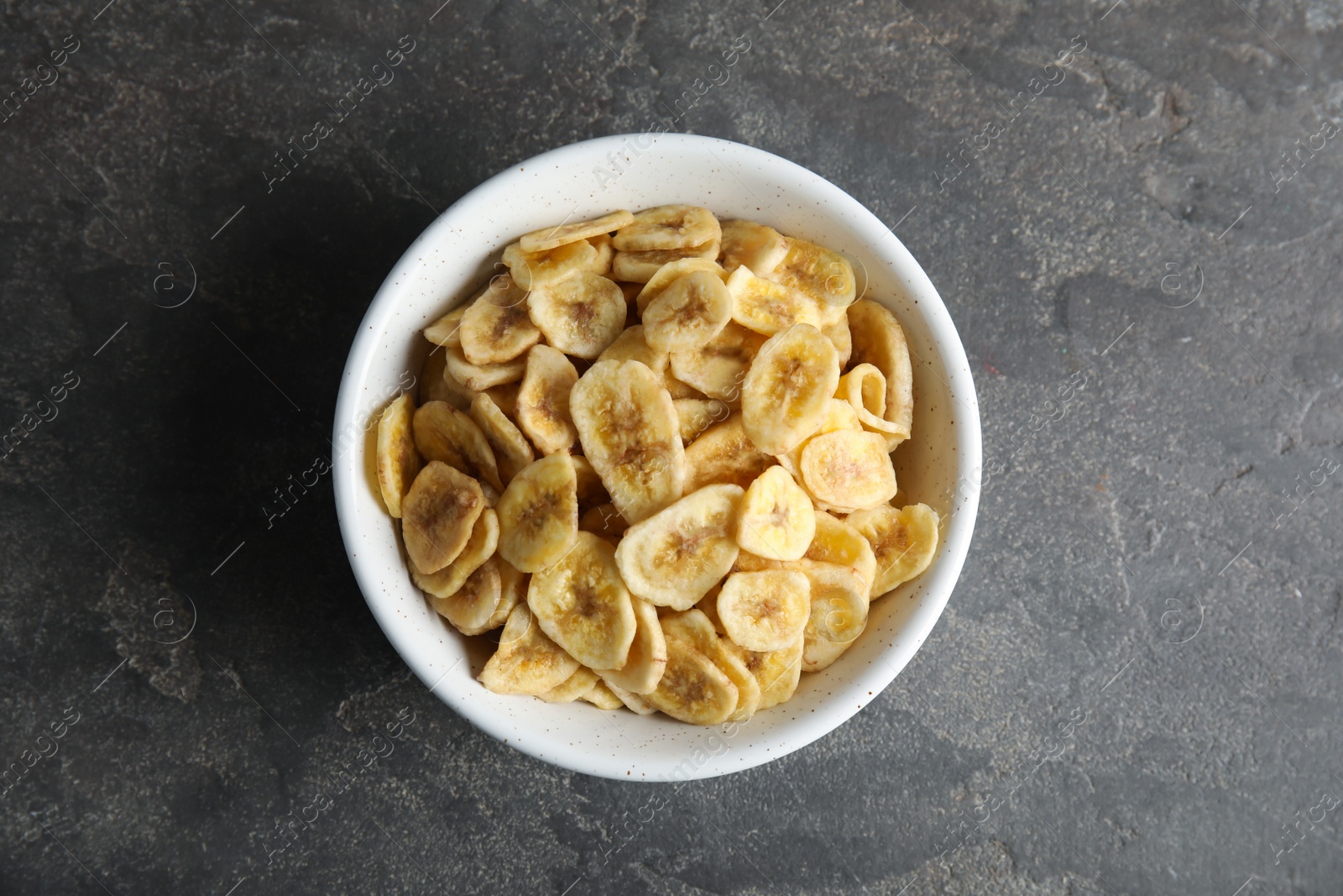 Photo of Bowl with sweet banana slices on grey background, top view. Dried fruit as healthy snack