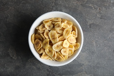 Photo of Bowl with sweet banana slices on grey background, top view. Dried fruit as healthy snack