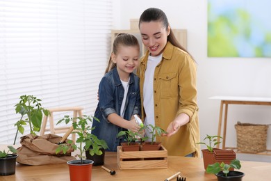 Photo of Mother and daughter spraying seedling in pots together at wooden table in room