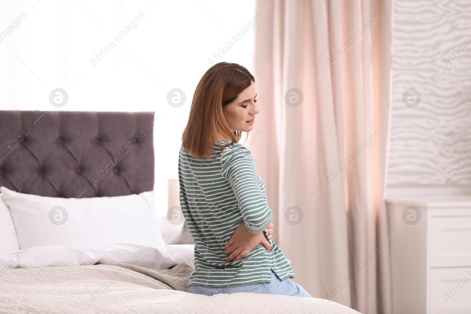 Photo of Young woman suffering from back pain at home