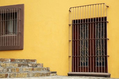 Yellow building with wooden door and window behind steel grilles outdoors