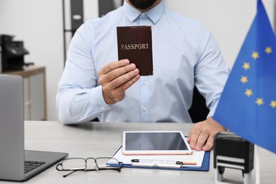 Photo of Immigration to European Union. Embassy worker with passport, tablet and documents at wooden table in office, closeup