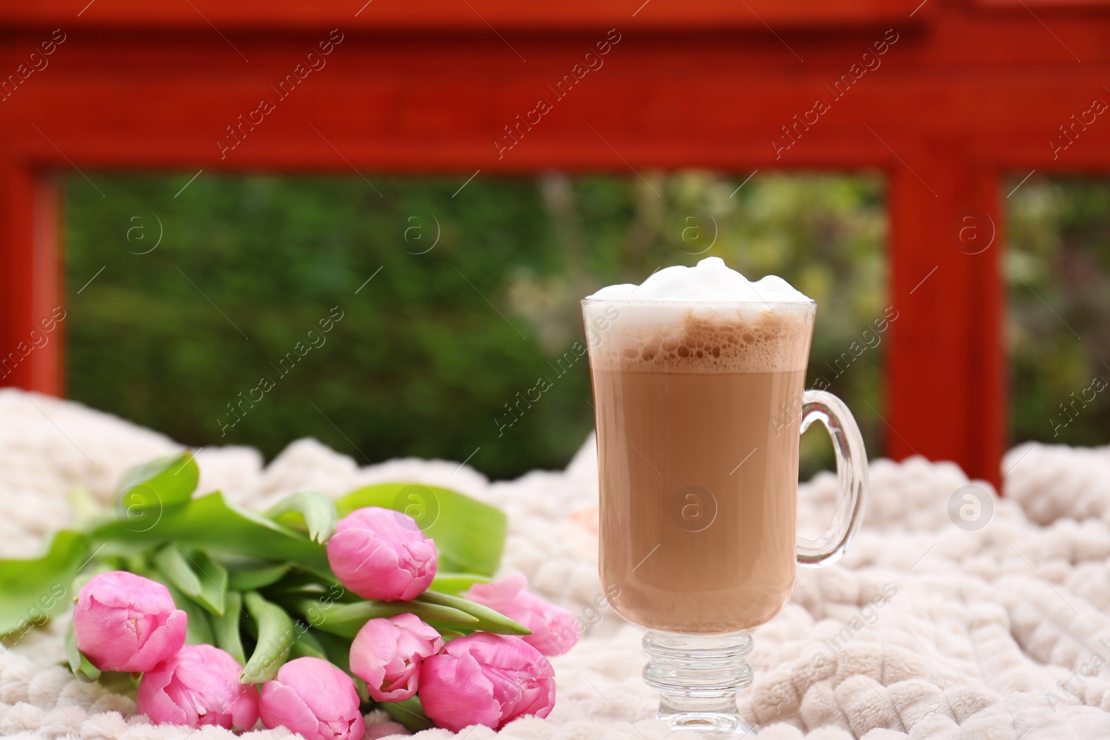 Photo of Glass of delicious cocoa and pink tulips on light blanket at terrace, space for text