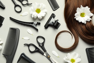 Flat lay composition with professional hairdresser tools, flowers and brown hair strand on light grey background