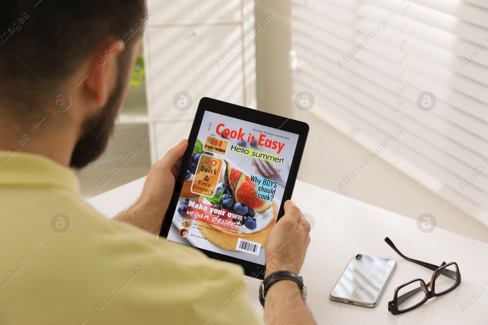 Photo of Man reading online magazine on tablet at white table, closeup