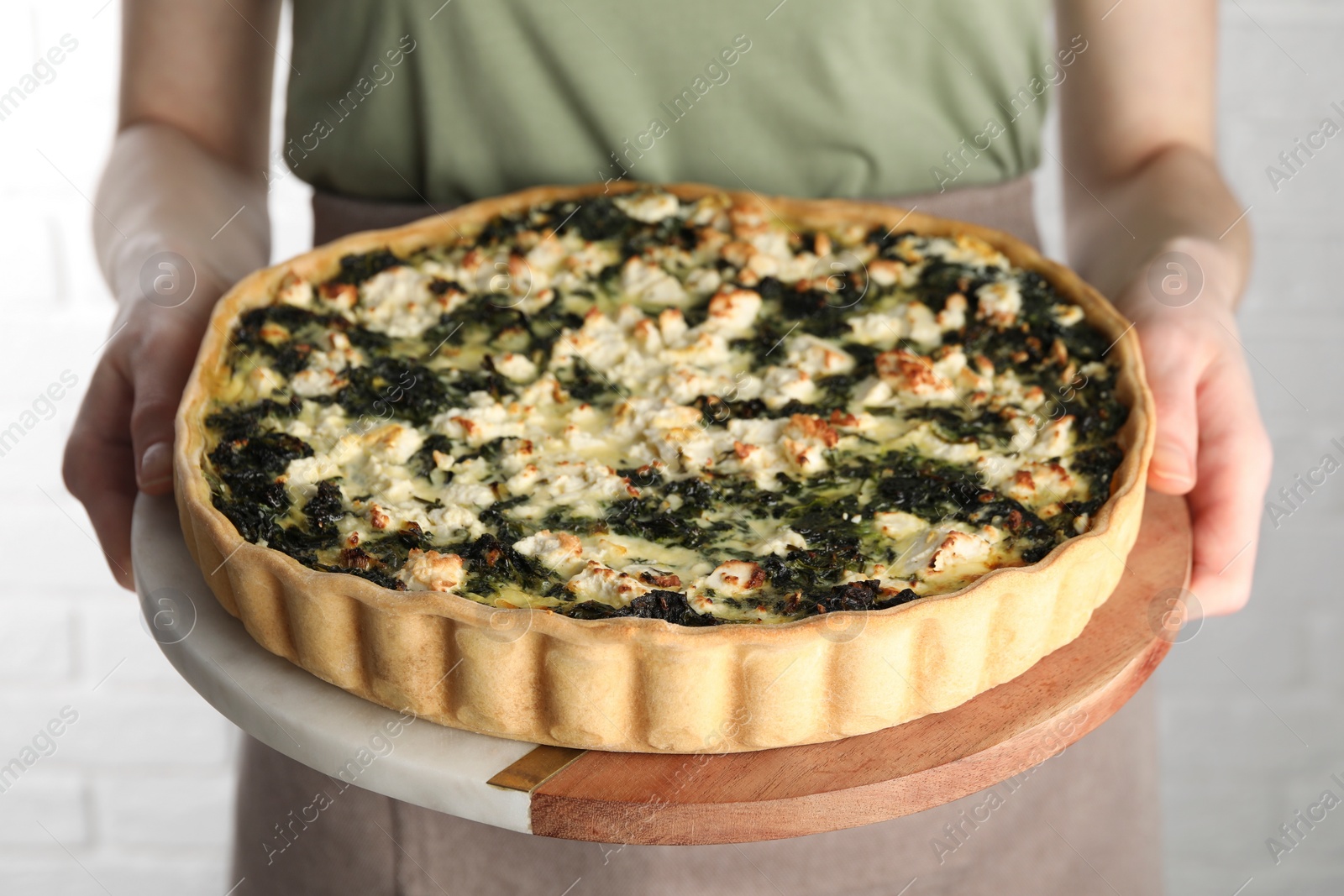 Photo of Woman holding delicious homemade spinach quiche on light background, closeup