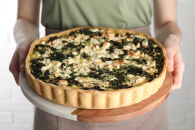 Photo of Woman holding delicious homemade spinach quiche on light background, closeup