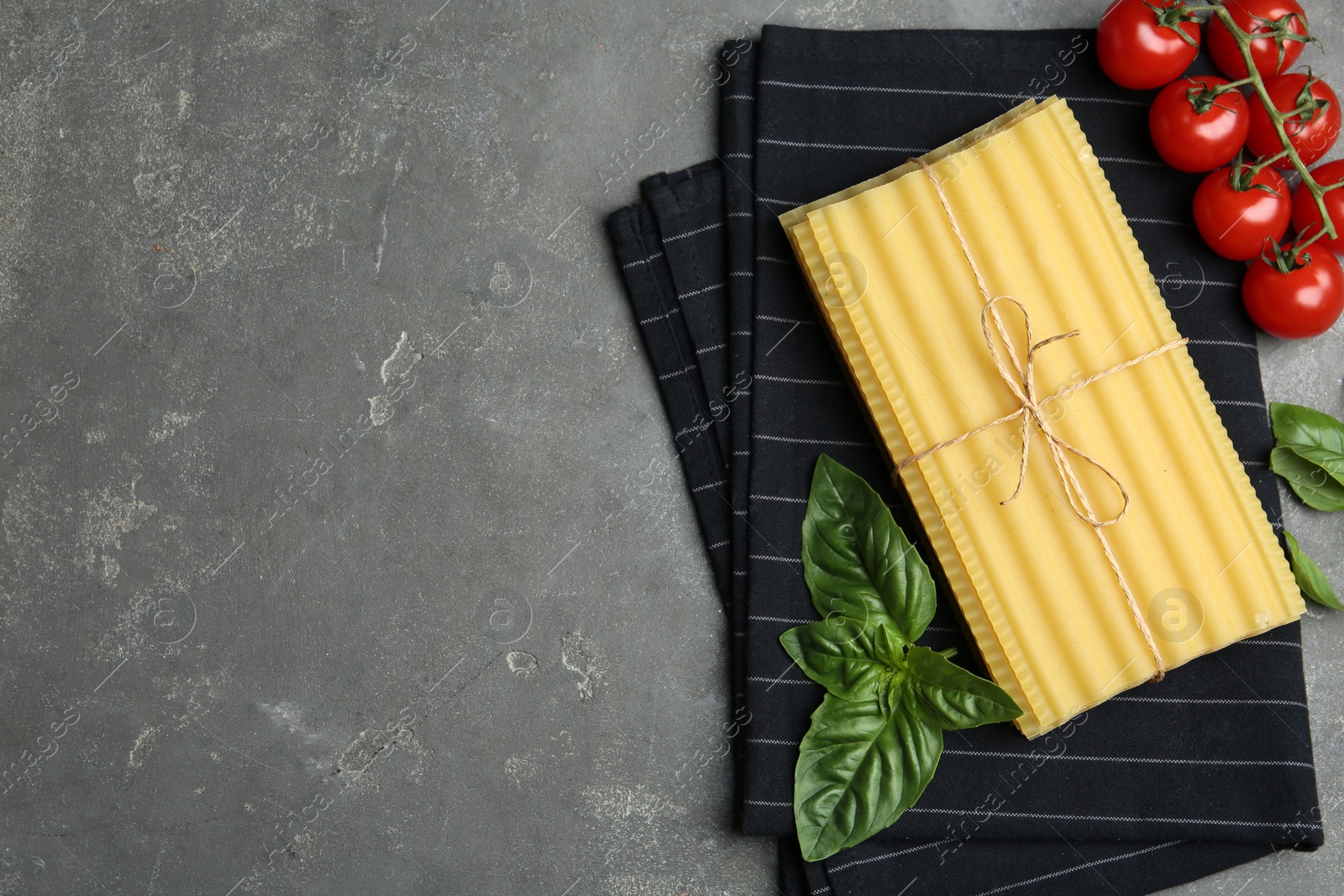 Photo of Uncooked lasagna sheets, cherry tomatoes and basil on grey table, flat lay. Space for text