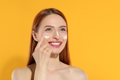 Photo of Beautiful young woman with sun protection cream on her face against orange background, space for text