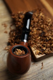 Smoking pipe with dry tobacco on wooden table, closeup