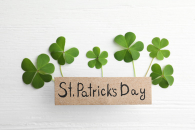 Clover leaves and card with text ST. PATRICK'S DAY on white wooden table, flat lay