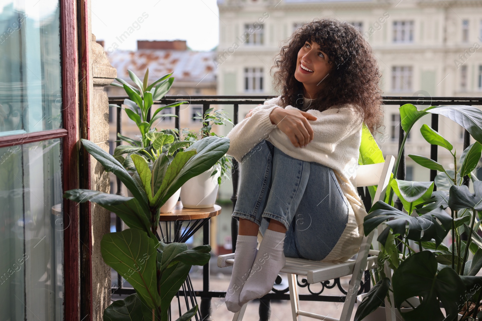 Photo of Beautiful young woman relaxing in chair surrounded by green houseplants on balcony