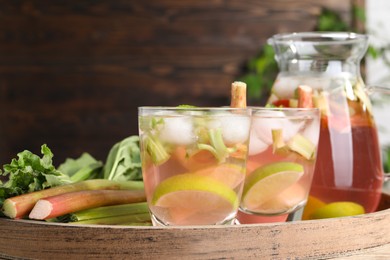 Photo of Tasty rhubarb cocktail with citrus fruits and stems on wooden board, closeup