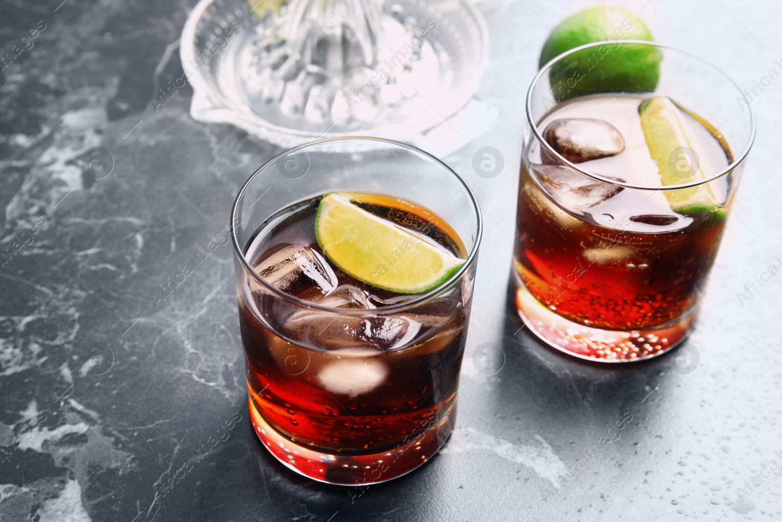 Photo of Glasses of cocktail with cola, ice and cut lime on marble background