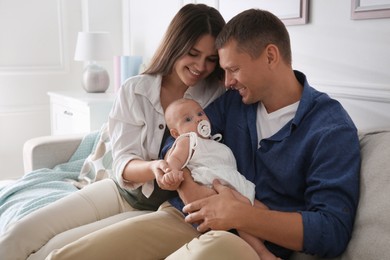 Happy couple holding their cute little baby with pacifier at home