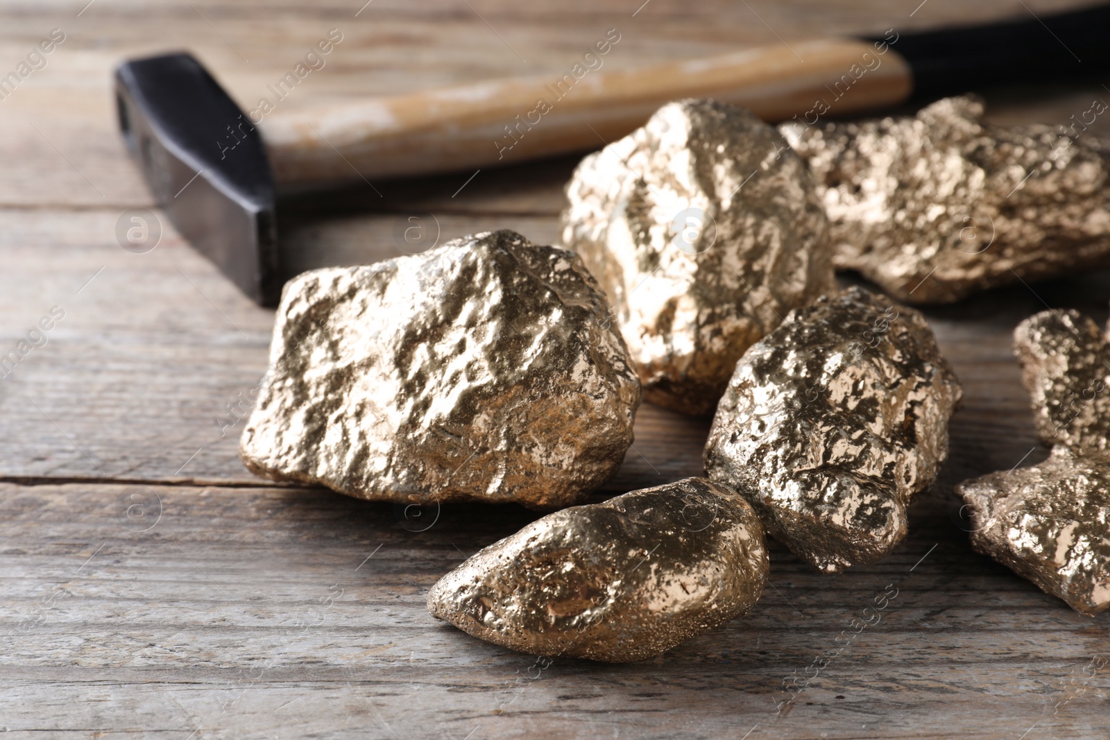 Photo of Pile of gold nuggets and hammer on wooden table, closeup