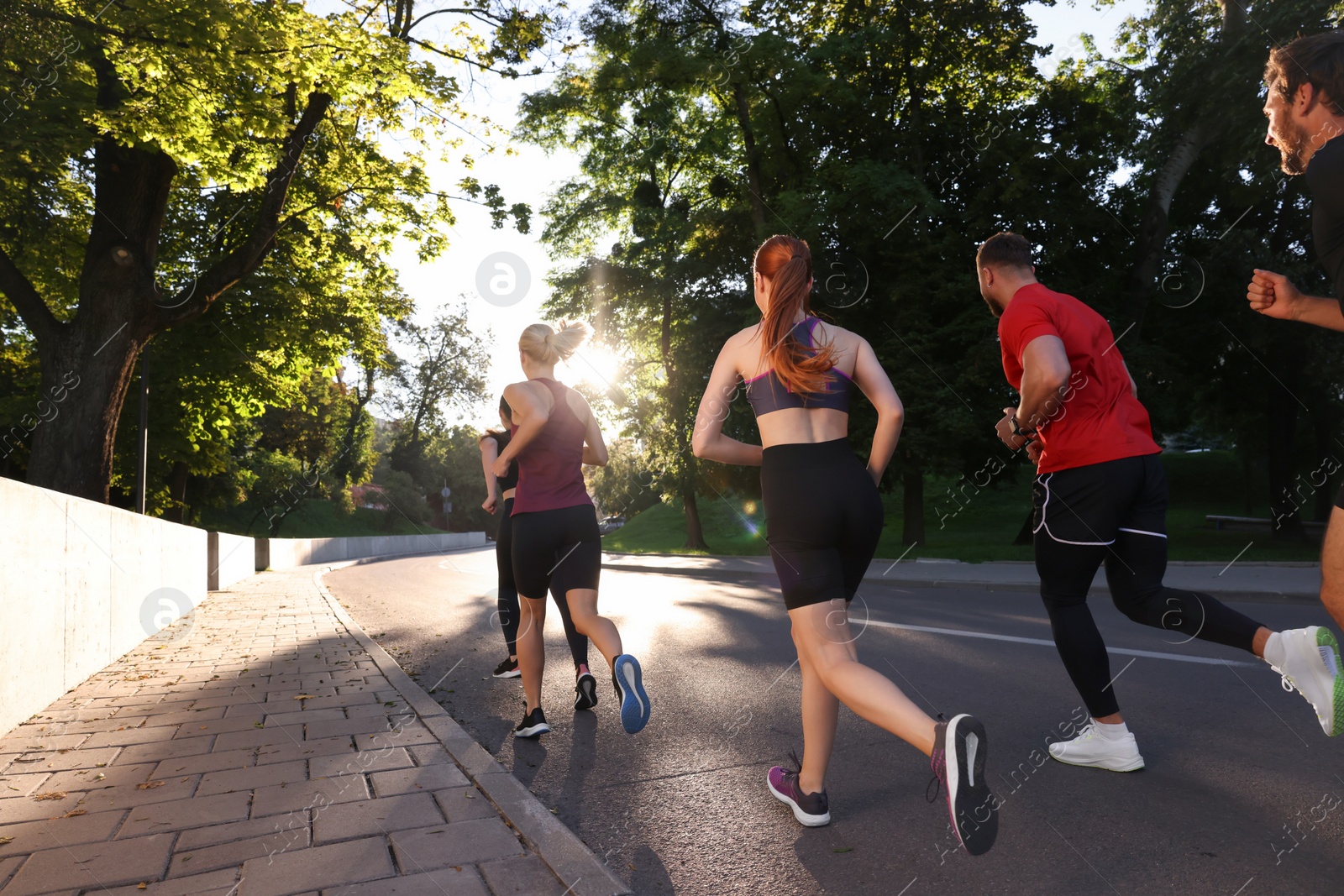 Photo of Group of people running outdoors on sunny day, back view