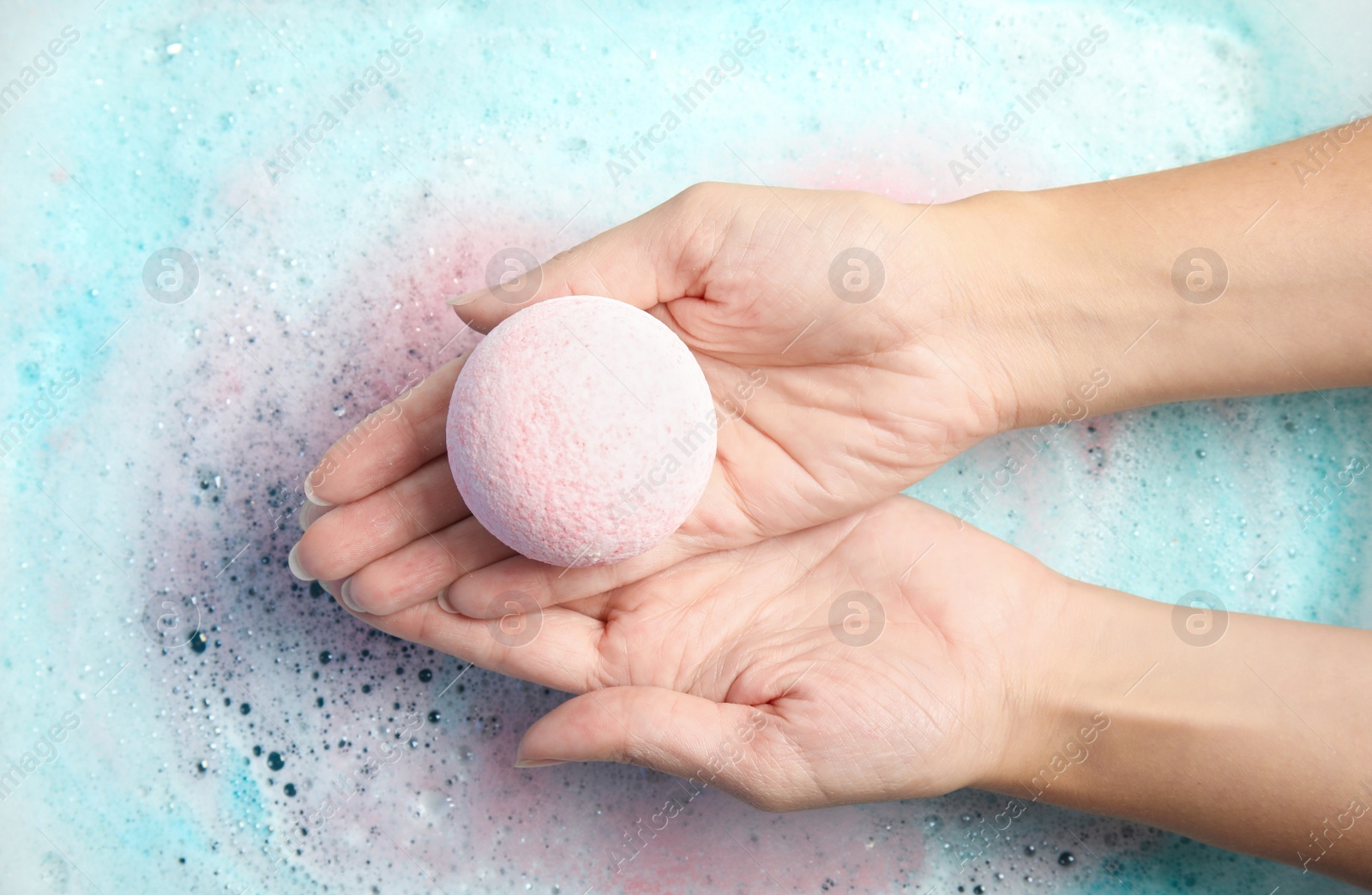 Photo of Woman holding color bath bomb over foam, top view