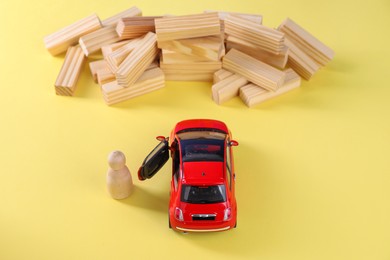 Photo of Overcoming barries for development and success. Wooden human figure near red toy car in front of blocks on yellow background