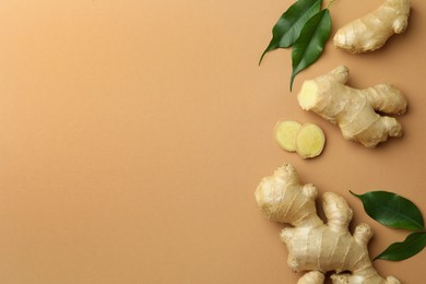 Photo of Fresh ginger with green leaves on light pale brown background, flat lay. Space for text