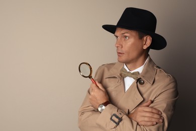 Photo of Male detective with magnifying glass on beige background. Space for text