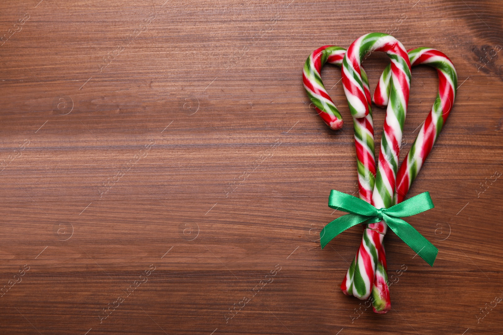 Photo of Bunch of sweet Christmas candy canes with bow on wooden table, top view. Space for text