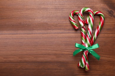 Photo of Bunch of sweet Christmas candy canes with bow on wooden table, top view. Space for text