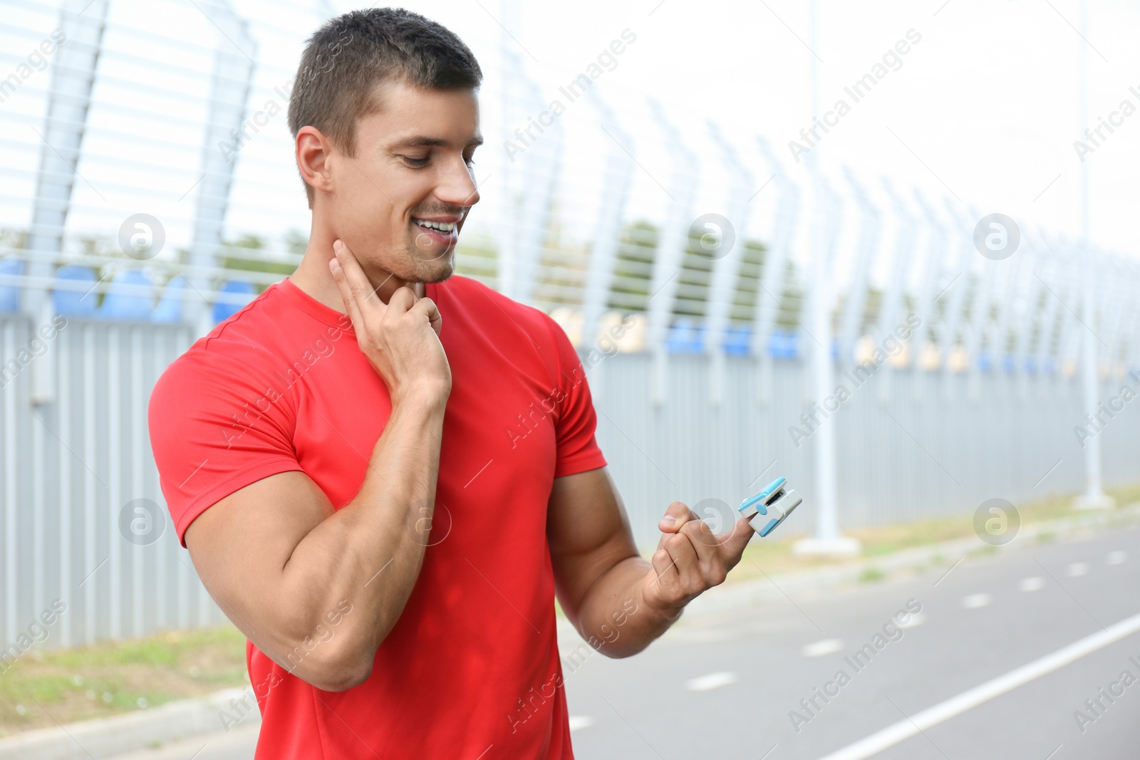 Photo of Young man checking pulse with medical device after training outdoors
