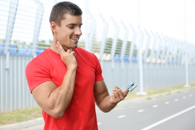 Young man checking pulse with medical device after training outdoors