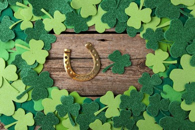 St. Patrick's day. Golden horseshoe and green decorative clover leaves on wooden table, flat lay