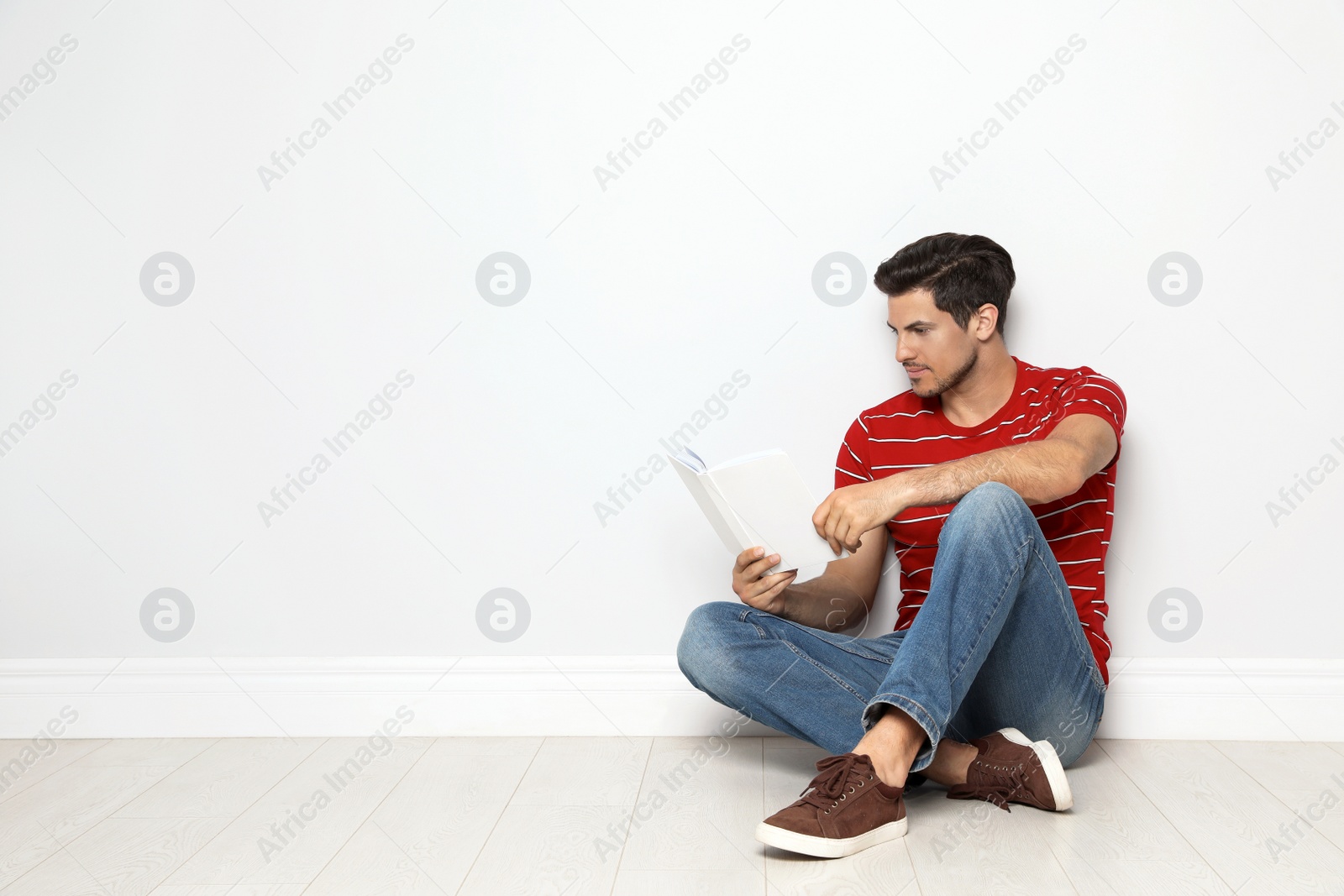 Photo of Handsome man reading book on floor near white wall, space for text