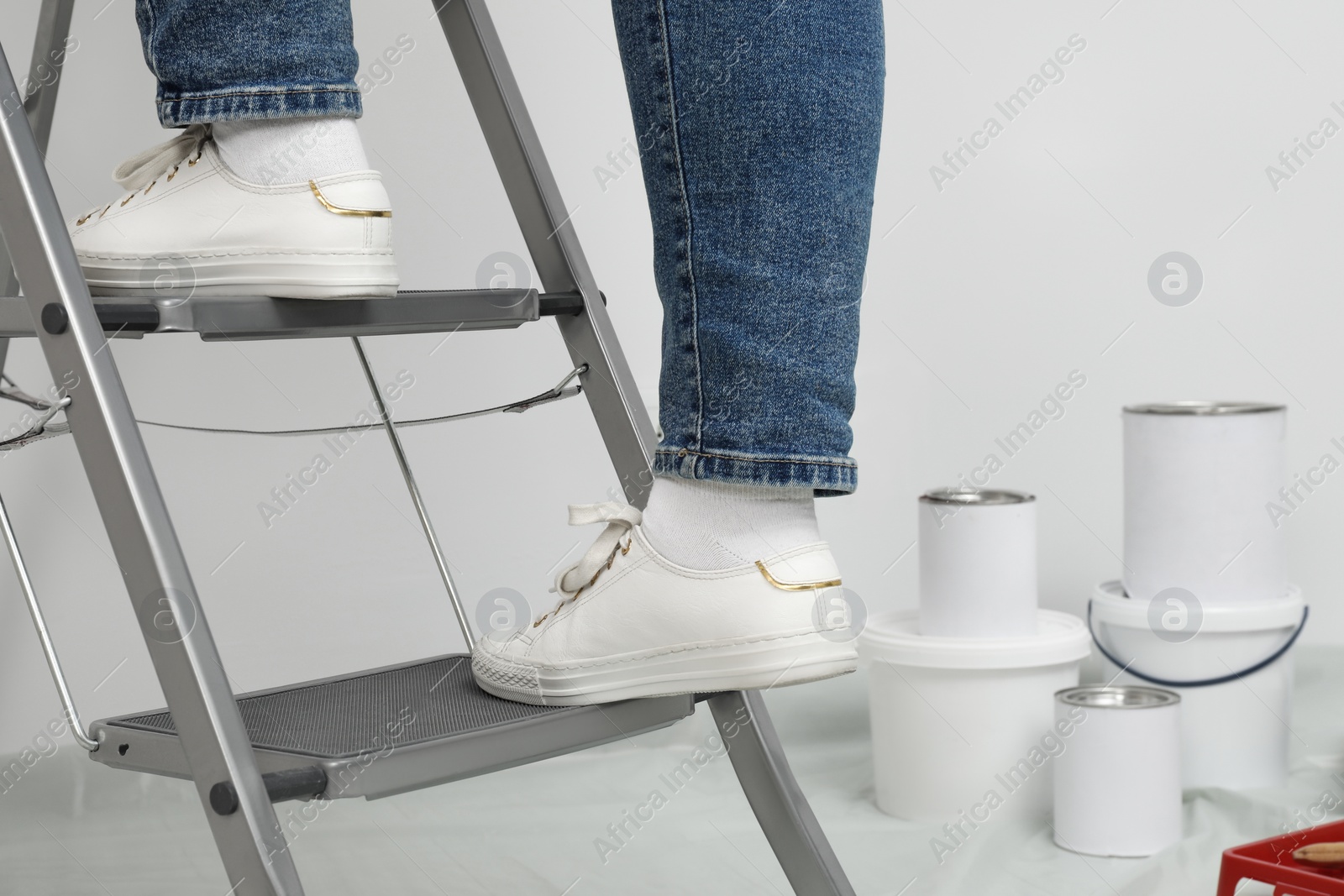 Photo of Woman climbing metallic folding ladder near painting tools indoors, closeup