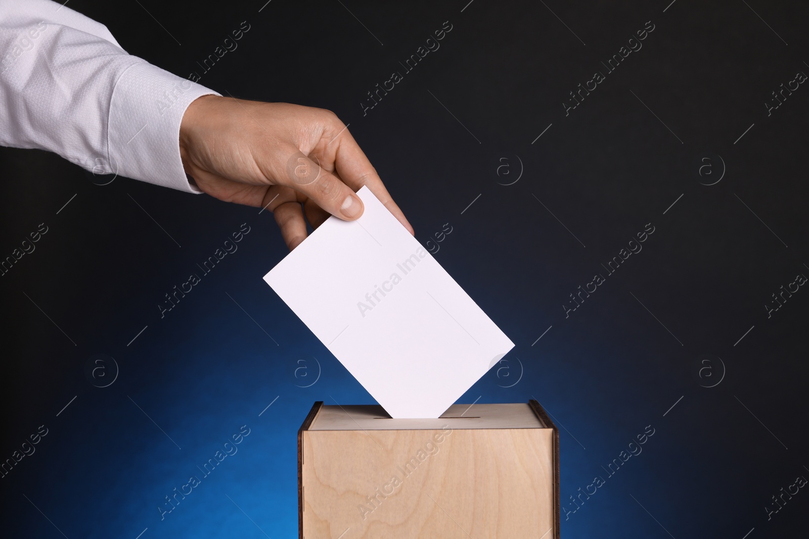 Photo of Man putting his vote into ballot box on dark blue background, closeup. Space for text