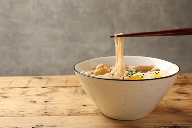 Photo of Noodle soup. Eating delicious ramen with chopsticks on wooden table, closeup. Space for text