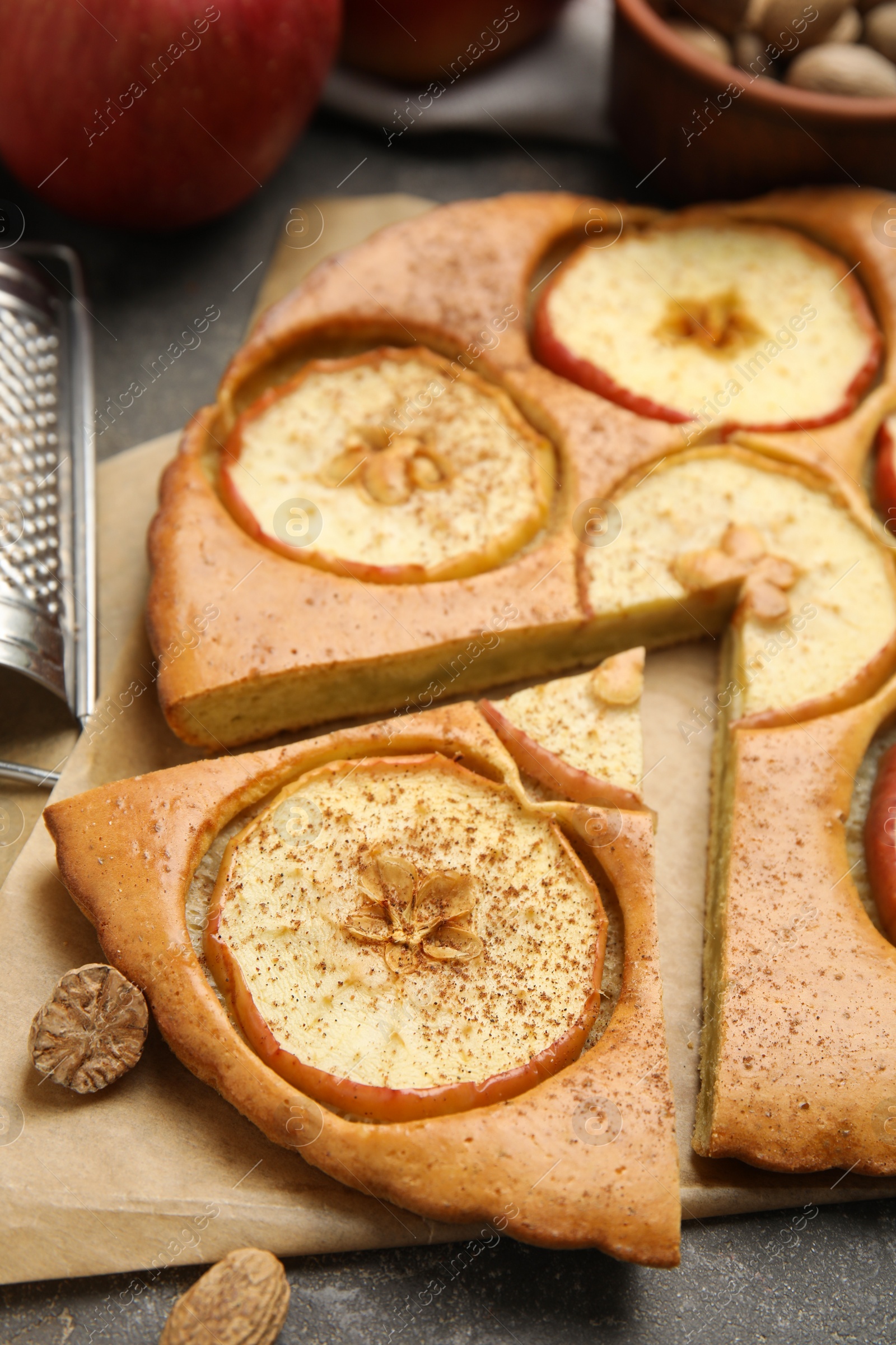 Photo of Tasty apple pie and nutmeg seeds on grey table, closeup