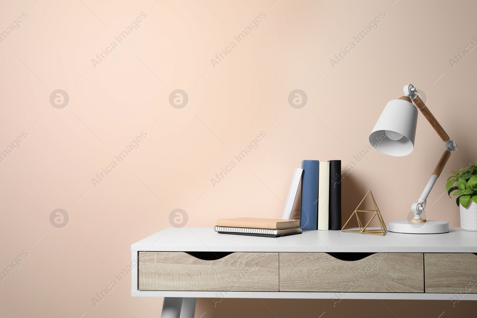 Photo of Stylish modern desk lamp, books and plant on table near beige wall indoors, space for text