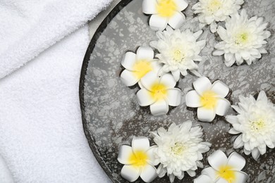 Photo of Bowl of water with flowers and towel on table, top view. Spa treatment