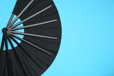 Photo of Stylish black hand fan on light blue background, top view. Space for text