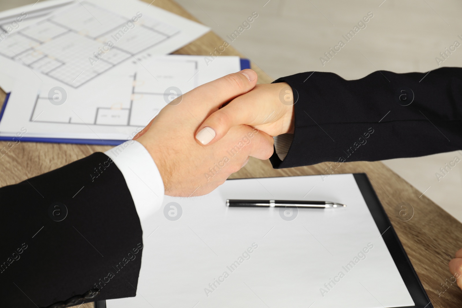 Photo of Real estate agent shaking hands with client at table in office, closeup